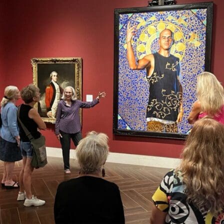 Tips for visiting the MFA St. Pete. Image: Woman docent speaking to group of people about a large painting of a young man. 